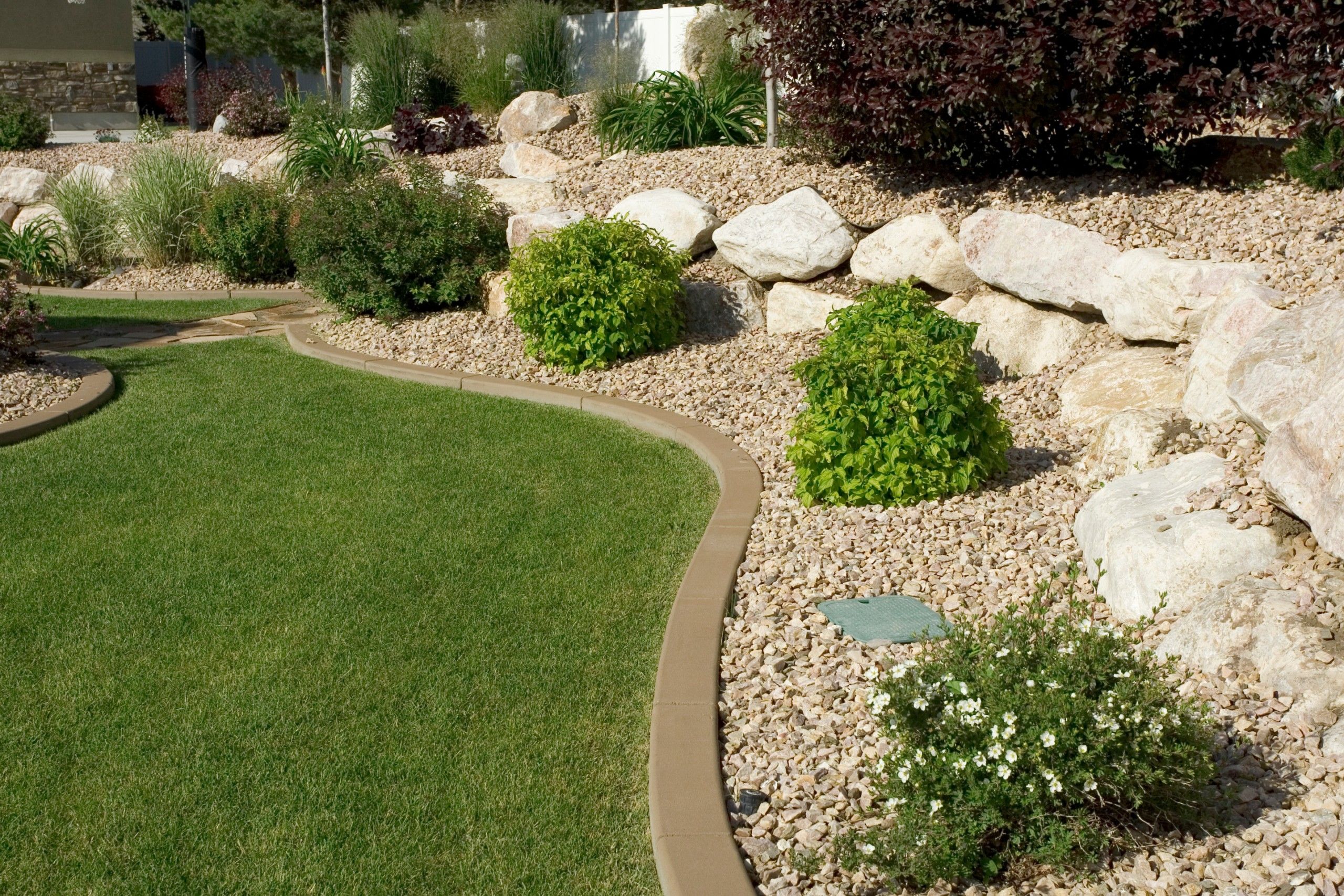 Neatly edged green lawn curving beside a landscaped bed of white river rock and shrubs