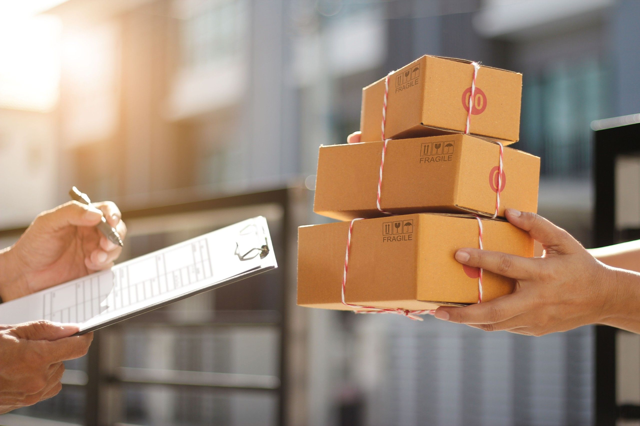 Courier handing a stack of tied cardboard boxes to a customer signing a clipboard